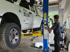 A white pickup truck on a lift at GMK Mechanical getting worked on by a mechanic in Lancaster, PA